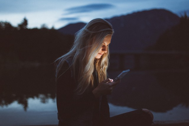 A woman looking a phone, outside by a lake in the dark