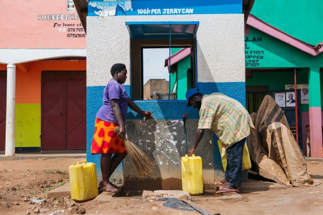 A man and a woman fill jerry cans with clean water from an outdoor tap.