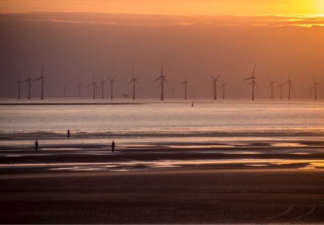 Sunset photograph of the sea with a wind farm in the distance