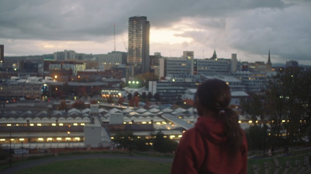 A woman looking over a view of Sheffield city centre at dawn.