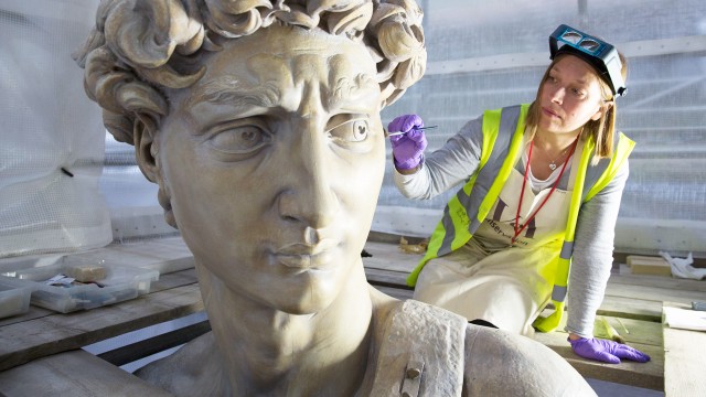 A woman in a high-vis jacket and purple gloves working on a large head of a statue